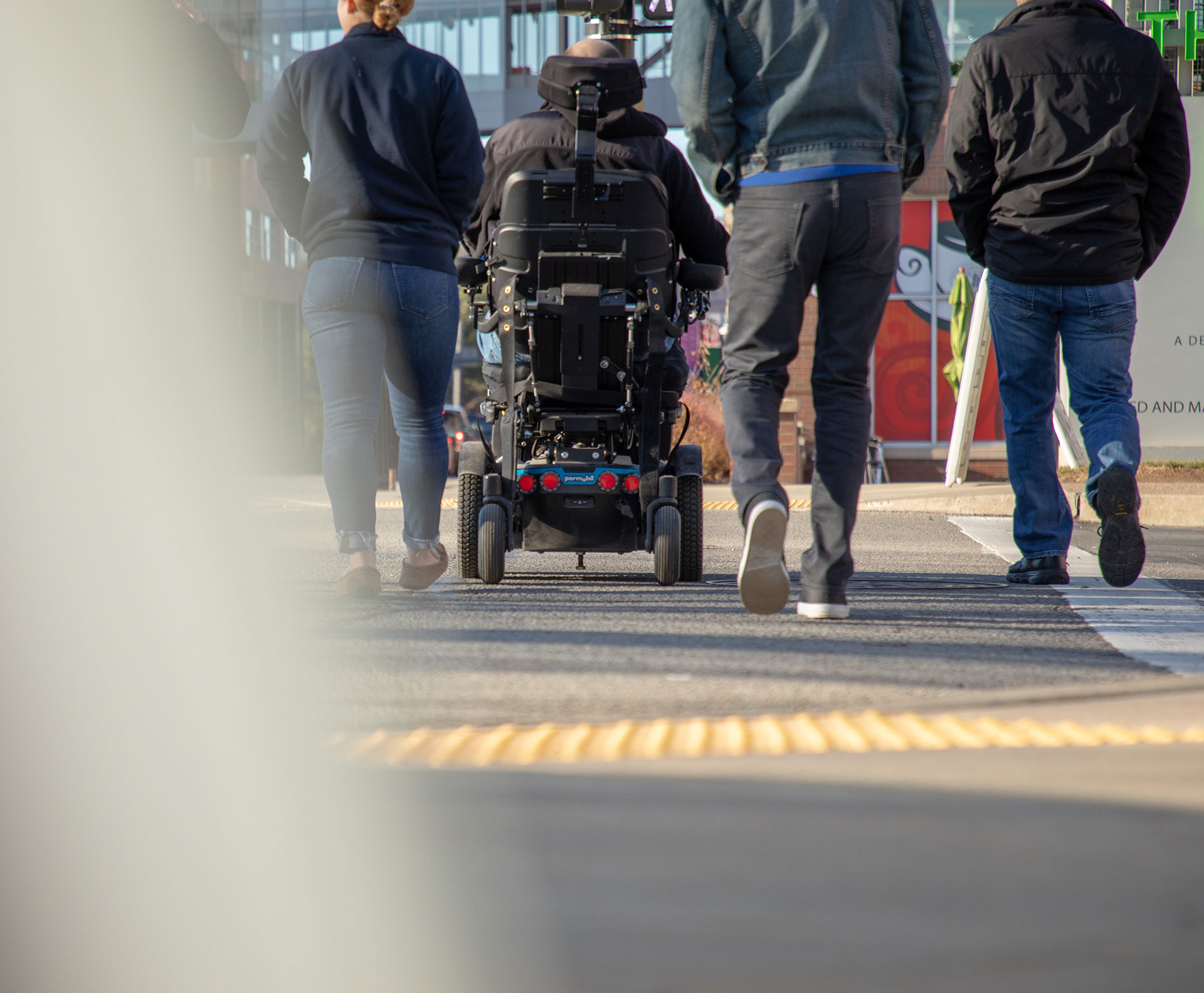 a group of pedestrians crossing the street together, one man uses a power wheelchair