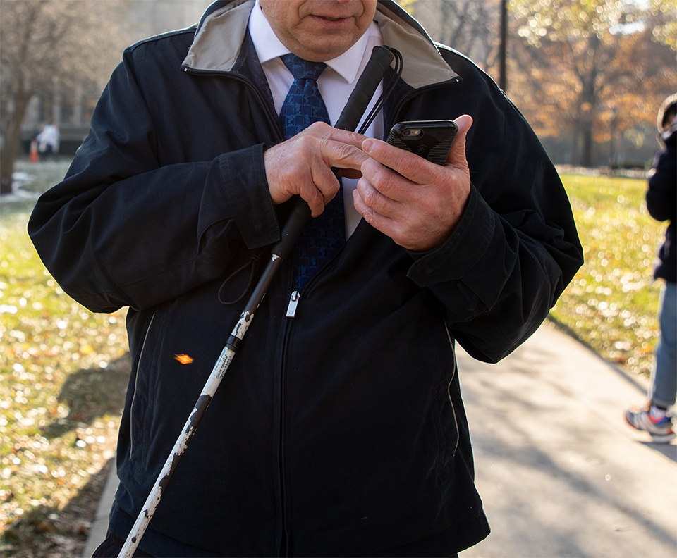 a male pedestrian with visual impairment uses pathVu navigation on his smartphone
